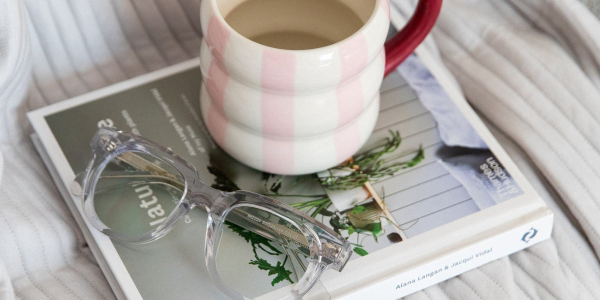 Stylish clear reading glasses on magazine with mug