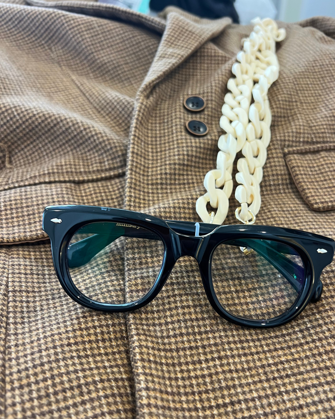 Black round stylish reading glasses for men and women with a chunky acrylic glasses chain, displayed on a brown and beige houndstooth jacket. Ministry of Sight