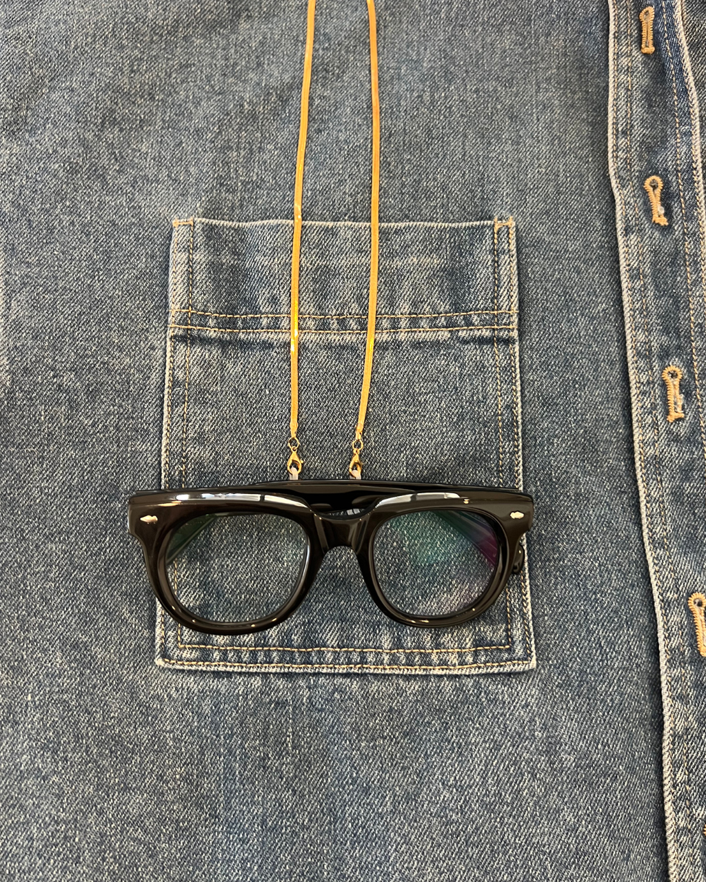 Black acetate round reading glasses hanging from gold flat lay snake chain glasses accessory 