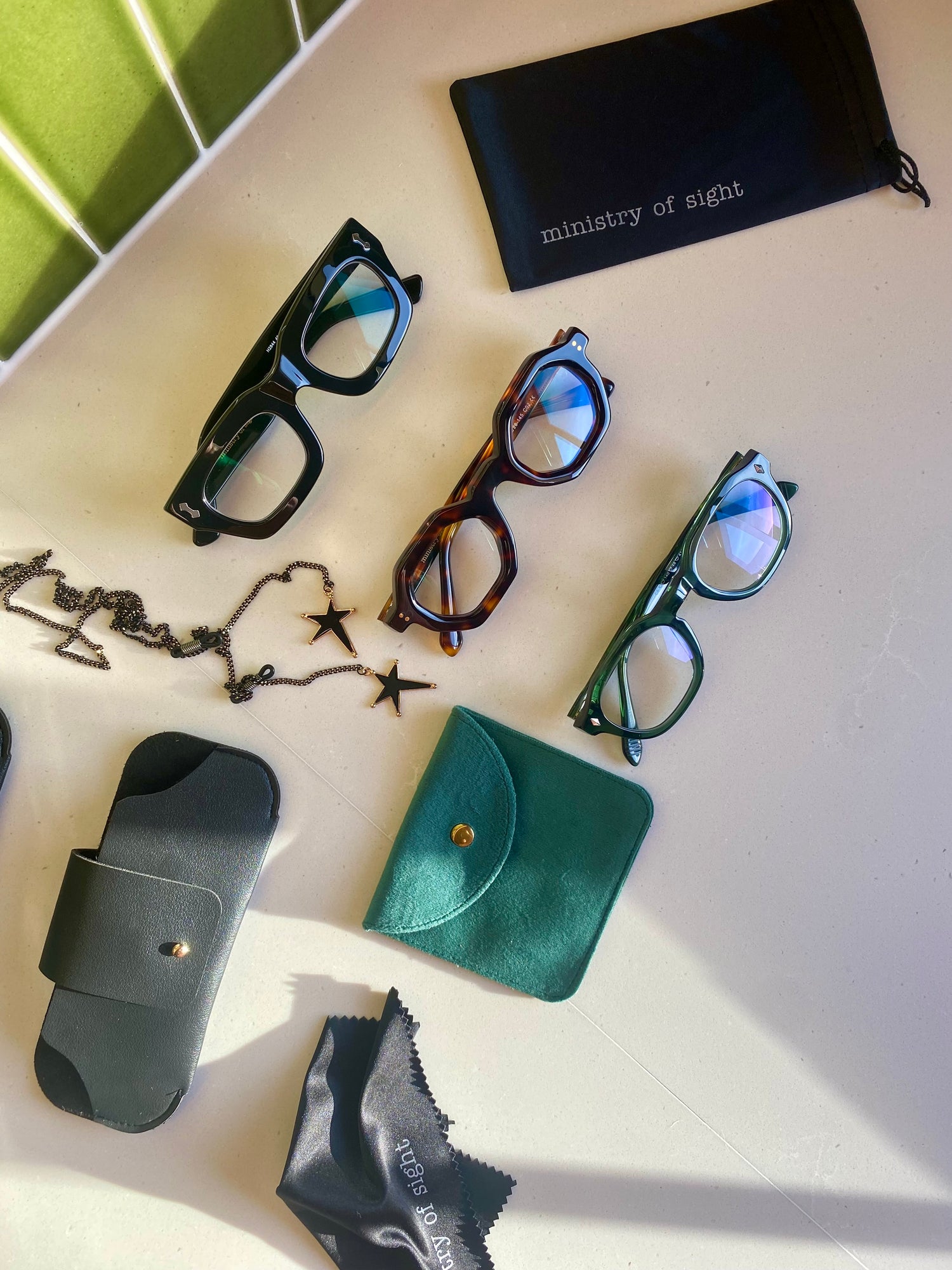 Flat Lay black reading glasses, tortoiseshell hexagonal reading glasses, green vintage reading glasses with glasses case, glasses pouch and glasses wipe. Glasses chain.