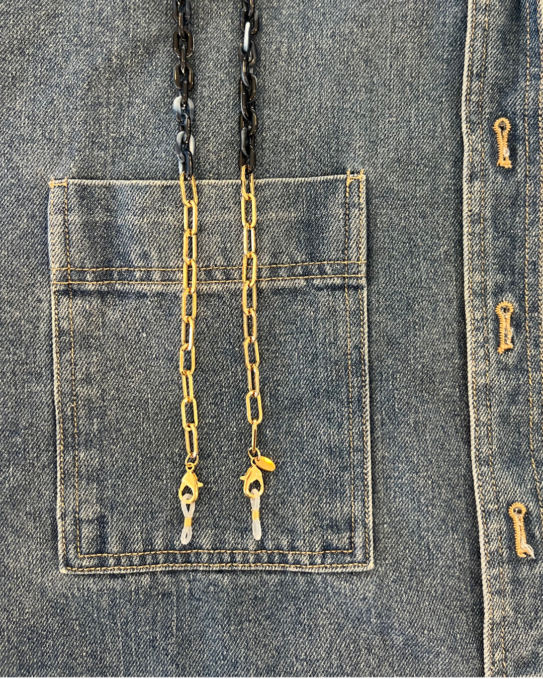 Close-up of a denim jacket with a front pocket, showing gold and navy blue glasses chain to keep your readers close. Look like jewellery. Ministry of sight