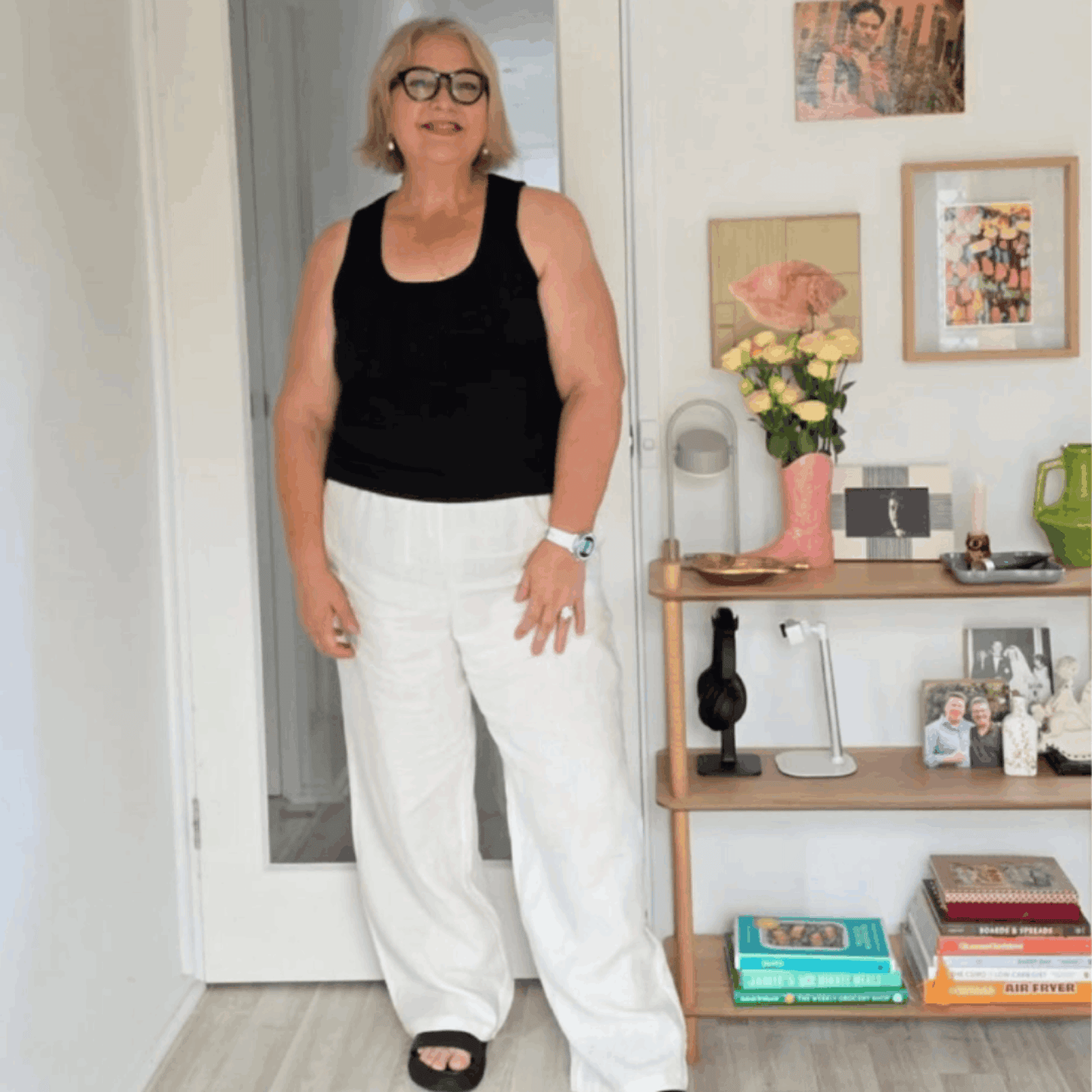 Australian woman over 50 in white pants and black top in stylish home wearing black frame flat top reading glasses - ministry of sight readers