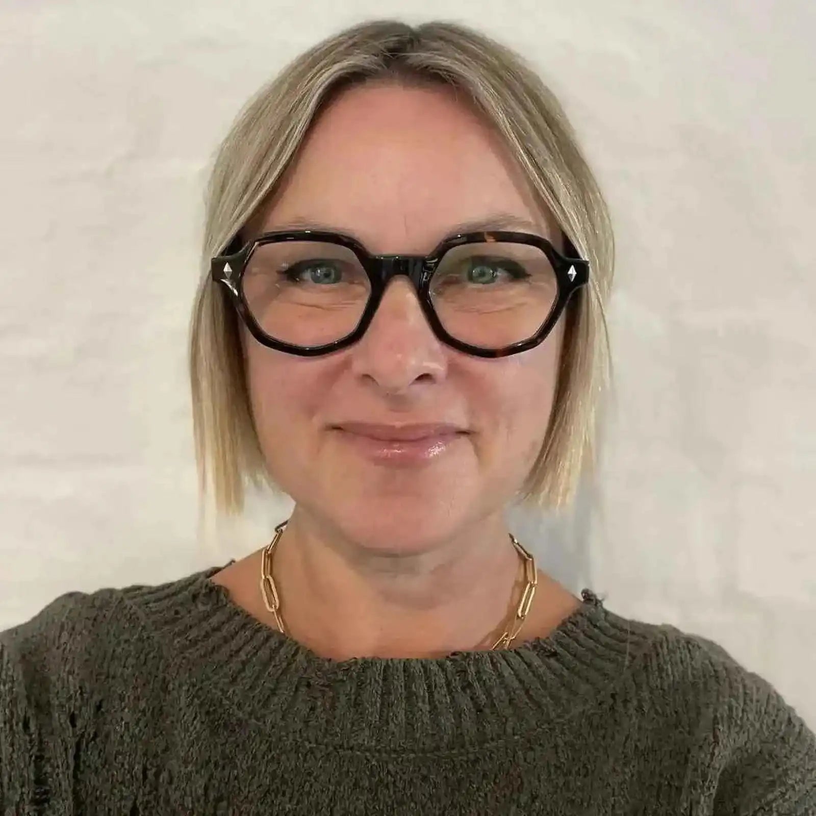 Australian woman in a green jumper with blonde hair wearing The Heptagon reading glasses. Geometric brown and black reading glasses - ministry of sight readers