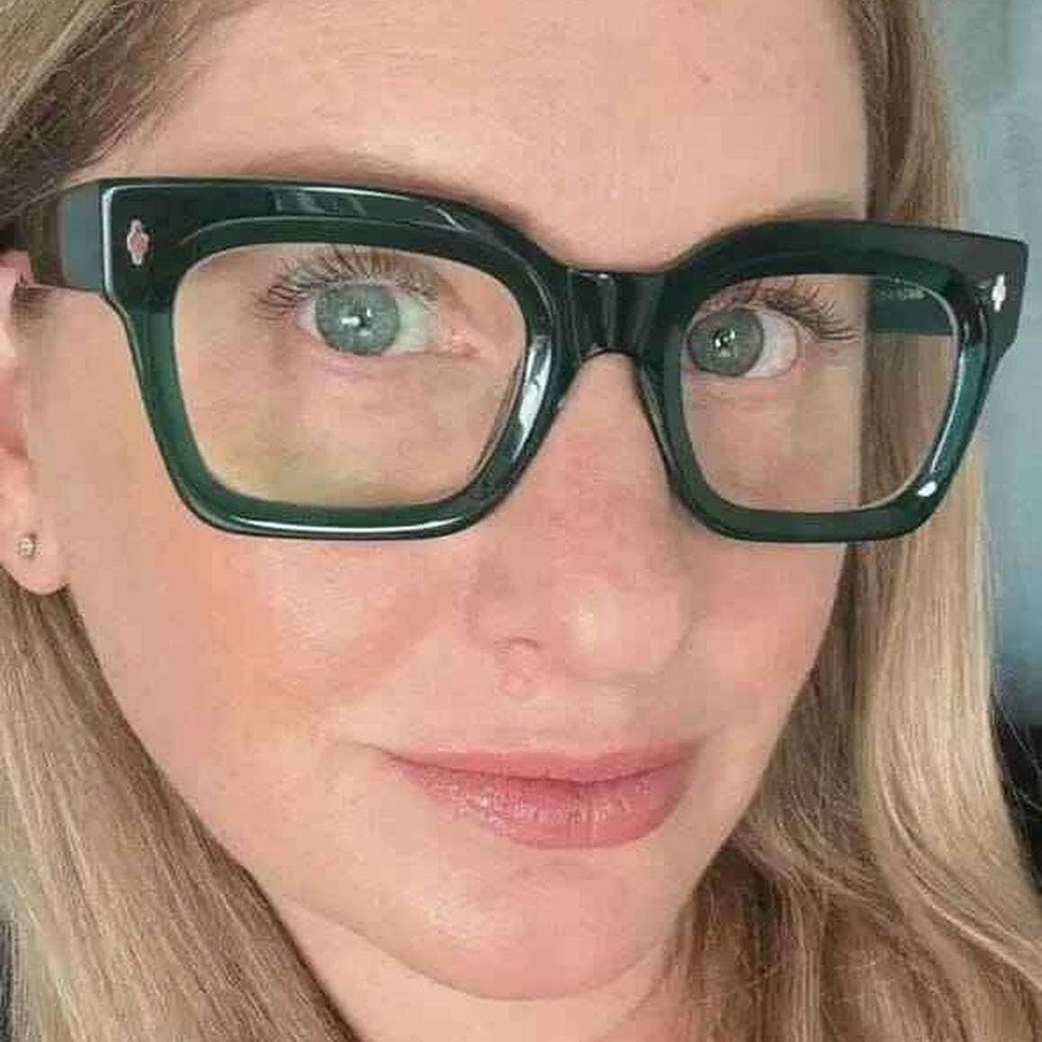 Close-up of a person wearing green reading glasses with a neutral background