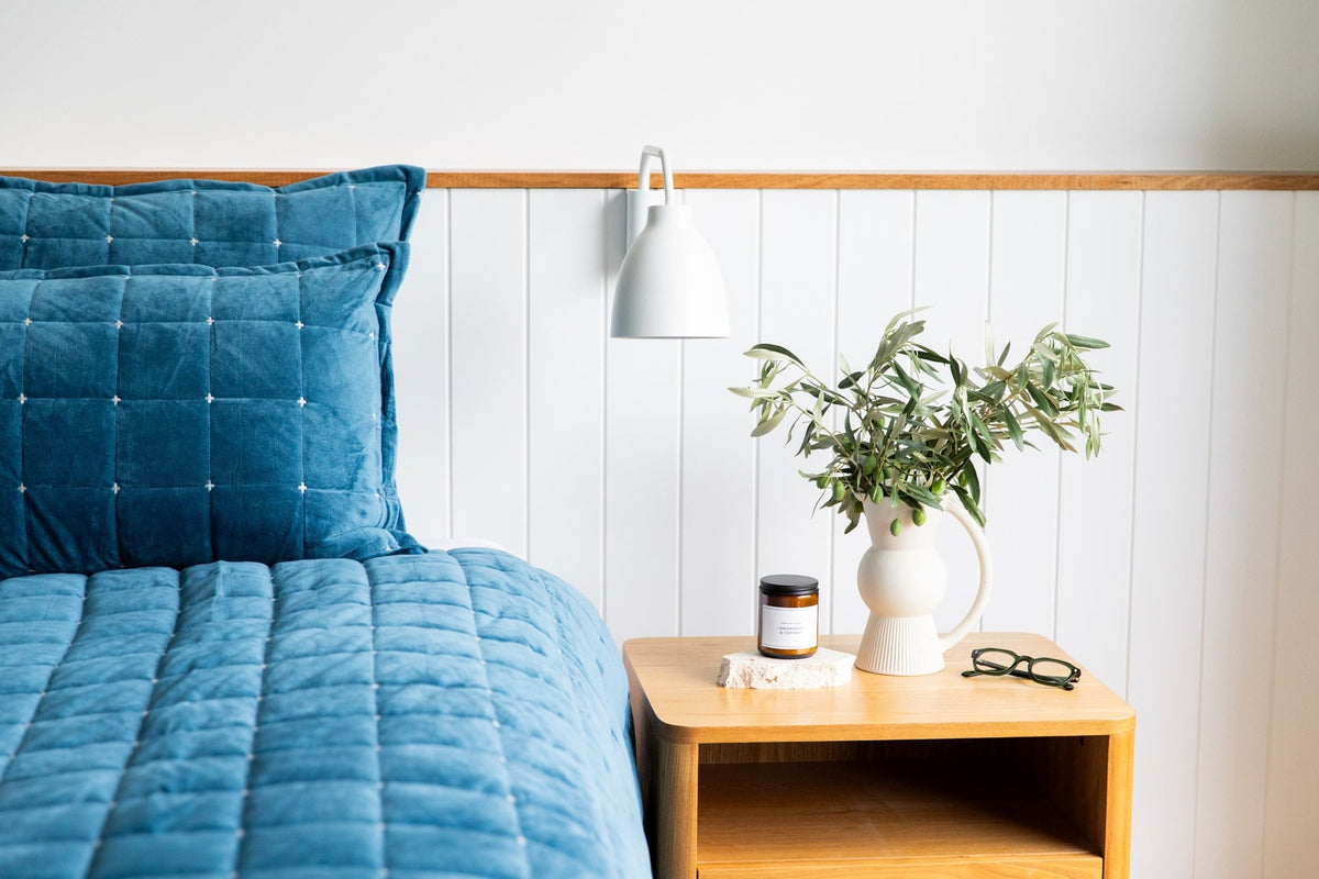 Blue quilted cover on a bed with a wooden nightstand and decorative items with readers